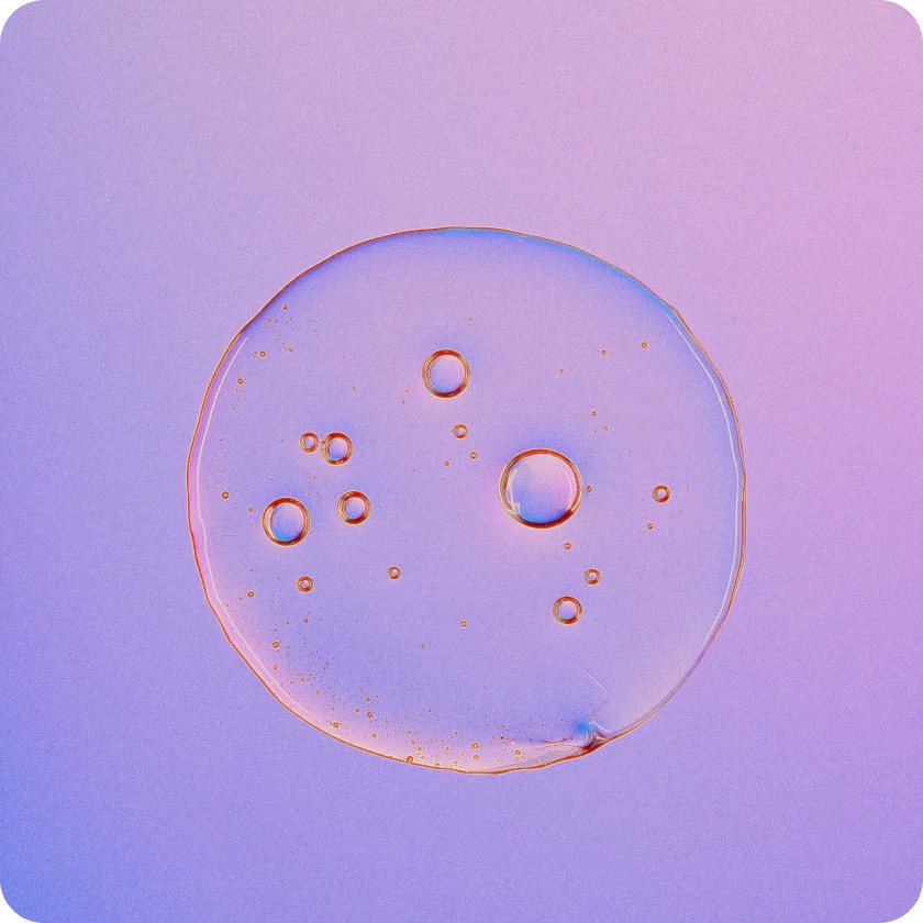 Close-up of a translucent liquid droplet with multiple small bubbles inside, set against a gradient purple and pink background.