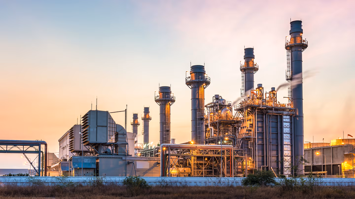 Industrial power plant with large chimneys and machinery at sunset.
