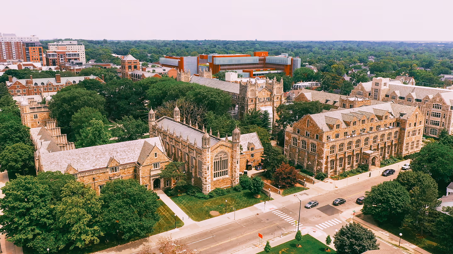Aerial view of a historic college campus with Gothic-style stone buildings surrounded by trees and roads.
